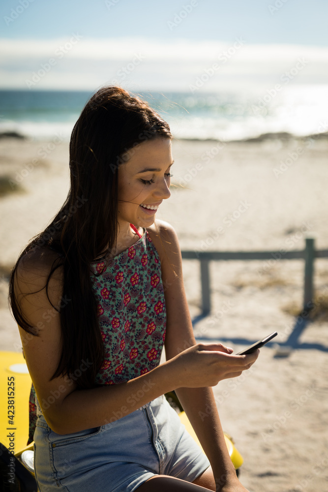 Happy caucasian woman sitting on beach buggy by the sea using smartphone