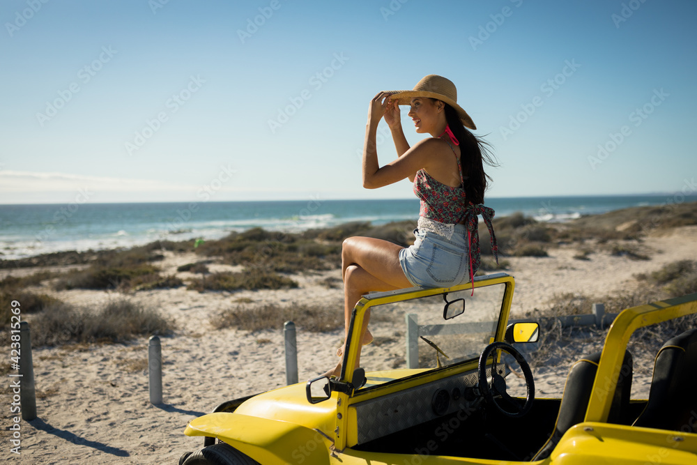 Happy caucasian woman sitting on beach buggy by the sea wearing straw hat looking toward sea Happy caucasian woman sitting on beach buggy by the sea wearing straw hat looking toward sea