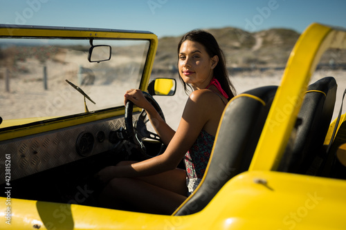 Happy caucasian woman sitting on beach buggy by the sea looking to camera