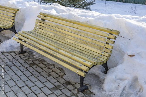 Snow-covered wooden bench in winter city park