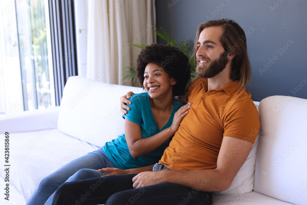 Obraz premium Happy diverse couple sitting on sofa embracing and smiling