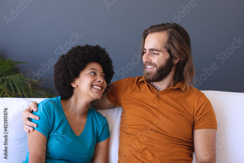 Happy diverse couple sitting on sofa embracing and smiling
