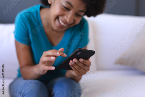 African american woman sitting on sofa using smartphone