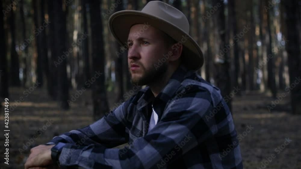 Young man with hat resting while hiking in the mountains or forest at sunset. Young man with hat resting while hiking in the mountains or forest at sunset.