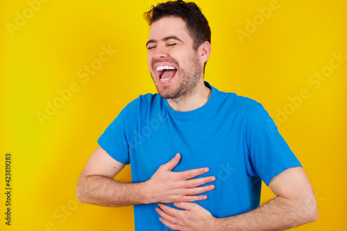 young handsome caucasian man wearing blue t-shirt against yellow background smiling and laughing hard out loud because funny crazy joke with hands on body.