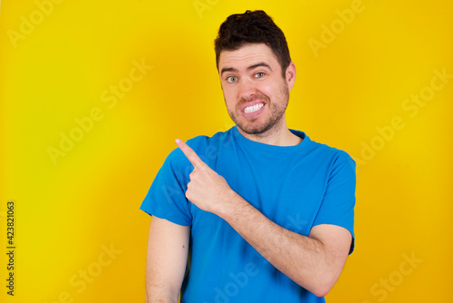 young handsome caucasian man wearing blue t-shirt against yellow background being confused and wonders about something. Holding hand on her head, uncertain with doubt. Pensive concept.