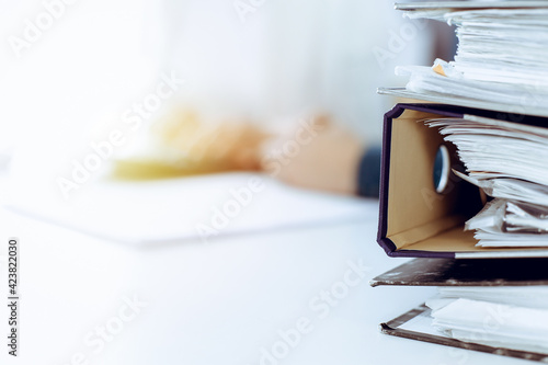 Binders with papers are waiting to be processed by business woman or bookkeeper working at the desk in office back in blur. Audit and tax concept