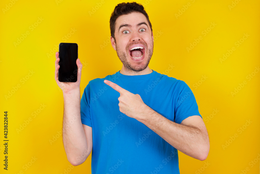 young handsome caucasian man wearing blue t-shirt against yellow background hold hand modern technology use touch face palm astonished impressed scream wow omg unbelievable unexpected young handsome caucasian man wearing blue t-shirt against yellow background hold hand modern technology use touch face palm astonished impressed scream wow omg unbelievable unexpected