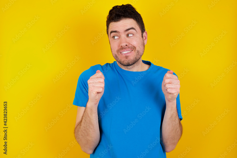 Photo of upbeat young handsome caucasian man wearing blue t-shirt against yellow background has fun and dances carefree wear being in perfect mood makes movements. Spends free time on disco party Photo of upbeat young handsome caucasian man wearing blue t-shirt against yellow background has fun and dances carefree wear being in perfect mood makes movements. Spends free time on disco party