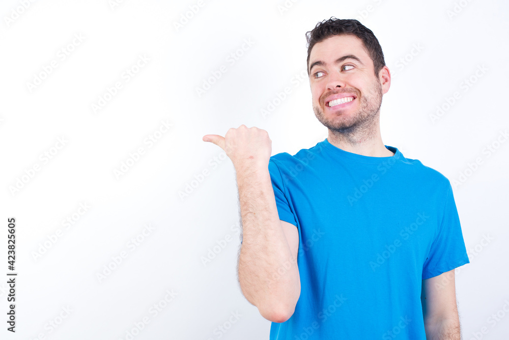 Charming young handsome caucasian man wearing blue t-shirt against white background looking at copy space having advertisements Charming young handsome caucasian man wearing blue t-shirt against white background looking at copy space having advertisements
