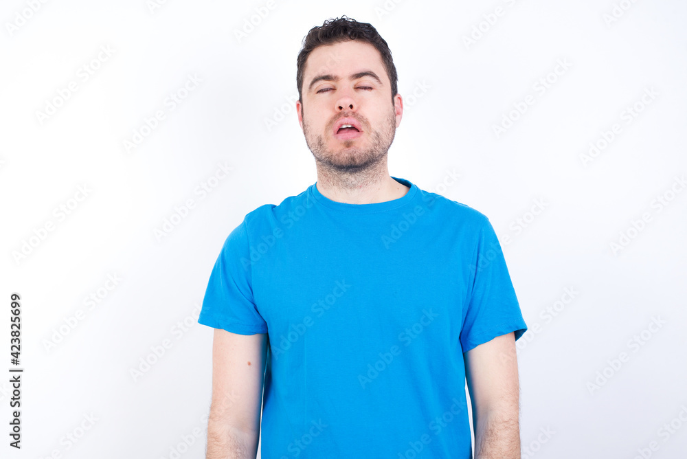young handsome caucasian man wearing blue t-shirt against white background looking sleepy and tired, exhausted for fatigue and hangover, lazy eyes in the morning. young handsome caucasian man wearing blue t-shirt against white background looking sleepy and tired, exhausted for fatigue and hangover, lazy eyes in the morning.
