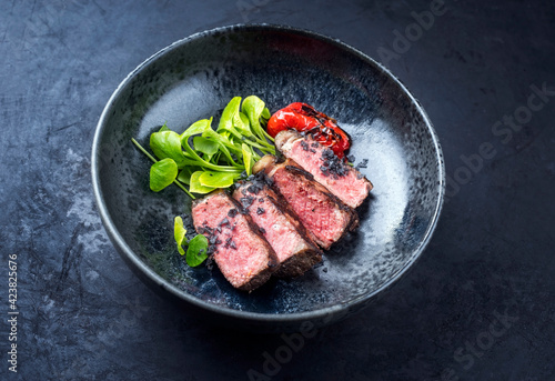 Modern style traditional dry aged sliced wagyu roast beef with fried onion rings served as top view on a rustic black board