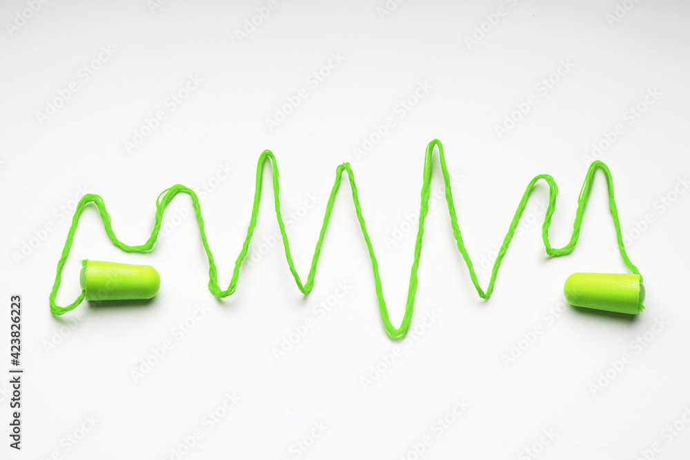 Green earplugs with wavy rope to show sound waves on white background Green earplugs with wavy rope to show sound waves on white background