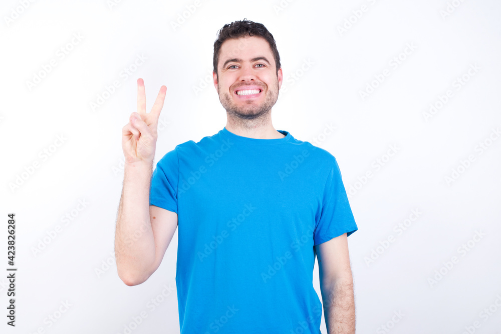 young handsome caucasian man wearing blue t-shirt against white background showing and pointing up with fingers number two while smiling confident and happy. young handsome caucasian man wearing blue t-shirt against white background showing and pointing up with fingers number two while smiling confident and happy.