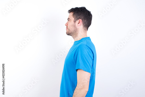 young handsome caucasian man wearing blue t-shirt against white background looking to side, relax profile pose with natural face with confident smile.