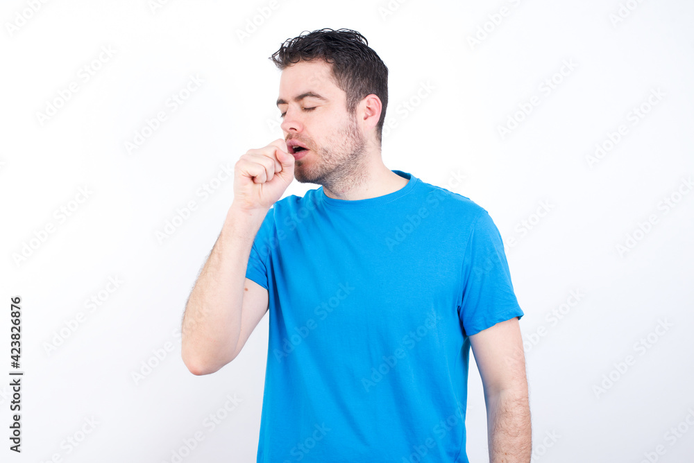 young handsome caucasian man wearing blue t-shirt against white background feeling unwell and coughing as symptom for cold or bronchitis. Healthcare concept. young handsome caucasian man wearing blue t-shirt against white background feeling unwell and coughing as symptom for cold or bronchitis. Healthcare concept.