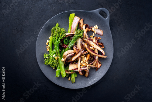 Modern style roasted rapini broccoli rabe and caramelized radicchio tardivo with pine nuts served as top view on a design plate with copy space photo