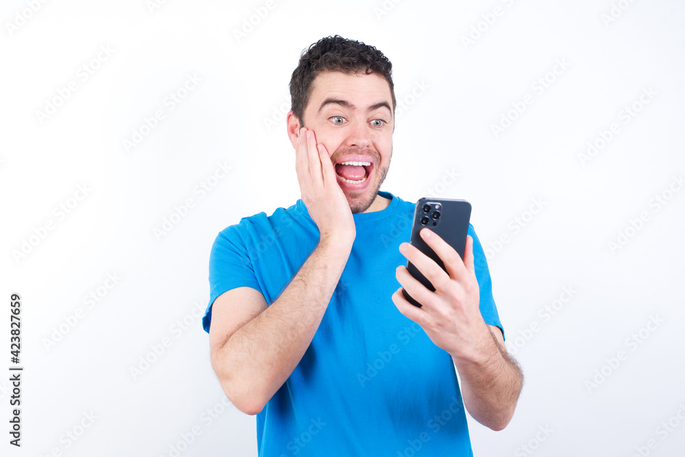 young handsome caucasian man wearing blue t-shirt against white background holding in hands cell reading sms using new app 5g young handsome caucasian man wearing blue t-shirt against white background holding in hands cell reading sms using new app 5g