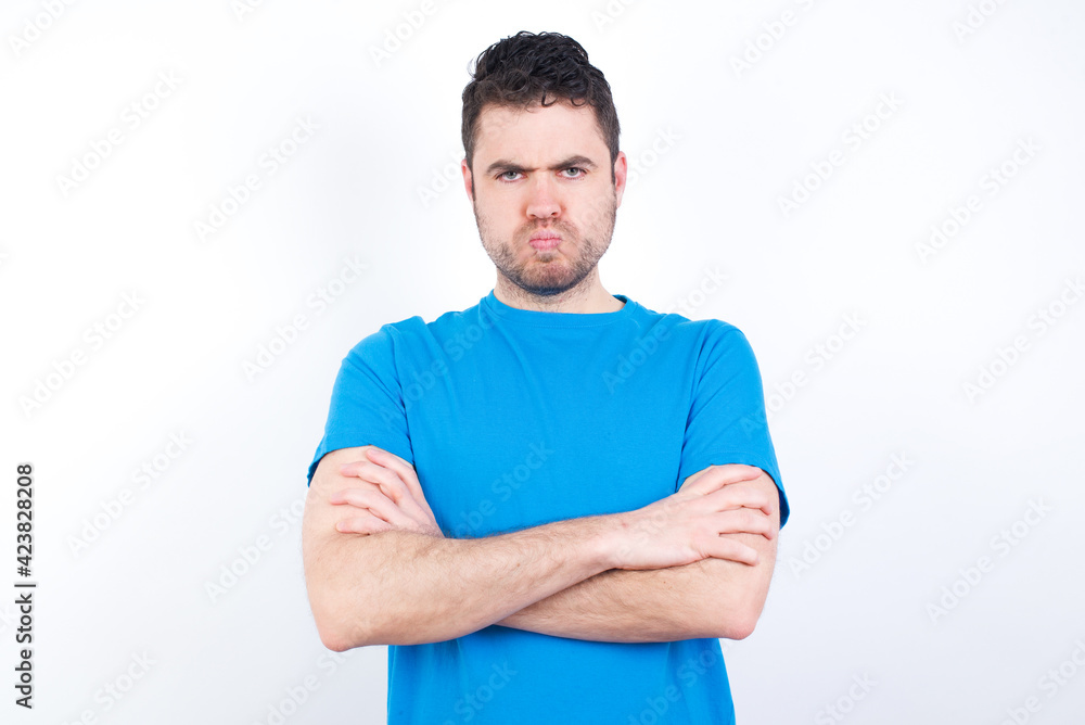 Gloomy dissatisfied young handsome caucasian man wearing white t-shirt against white background looks with miserable expression at camera from under forehead, makes unhappy grimace Gloomy dissatisfied young handsome caucasian man wearing white t-shirt against white background looks with miserable expression at camera from under forehead, makes unhappy grimace