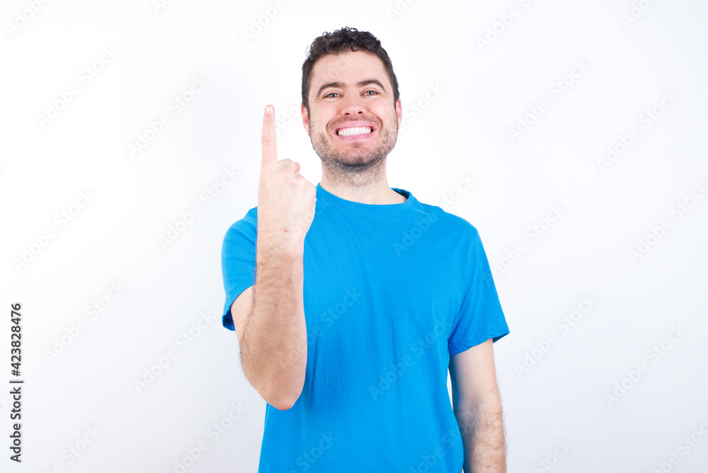 young handsome caucasian man wearing white t-shirt against white background smiling and looking friendly, showing number one or first with hand forward, counting down young handsome caucasian man wearing white t-shirt against white background smiling and looking friendly, showing number one or first with hand forward, counting down