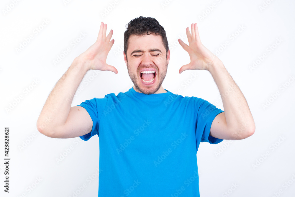 young handsome caucasian man wearing white t-shirt against white background goes crazy as head goes around feels stressed because of horrible situation young handsome caucasian man wearing white t-shirt against white background goes crazy as head goes around feels stressed because of horrible situation