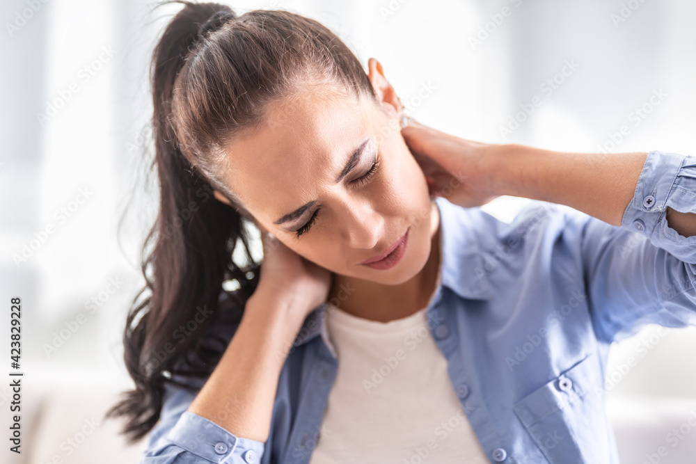 Neck pain of a woman at home with painful facial expression Neck pain of a woman at home with painful facial expression