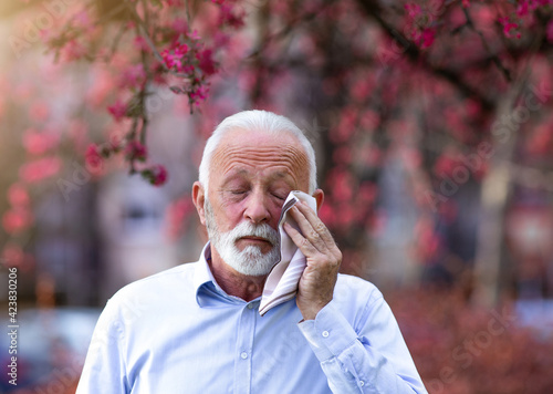 Old man rubbing eyes because of pollen allergy in spring