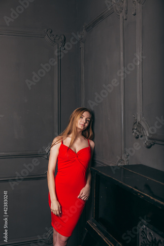 beautiful girl in a red dress stands against a dark wall
