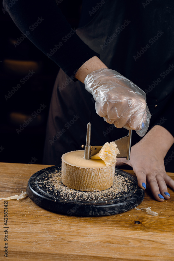 Shaving tete de moine cheese using girolle knife. Variety of Swiss  semi-hard cheese made from unpasteurized cows milk, the name Monks head  Stock Photo