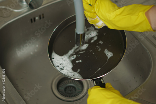 A woman in yellow rubber gloves washes a frying pan
