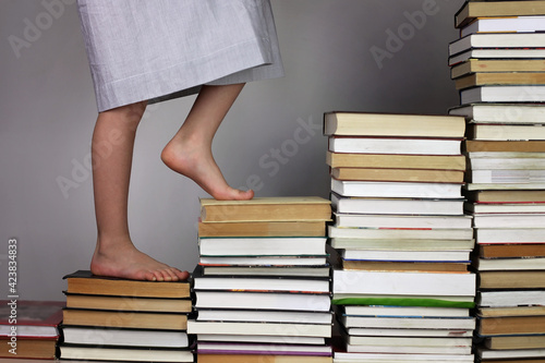 Preschool girl going up the stairs of books from one education level to another, studio shot, study and education concept