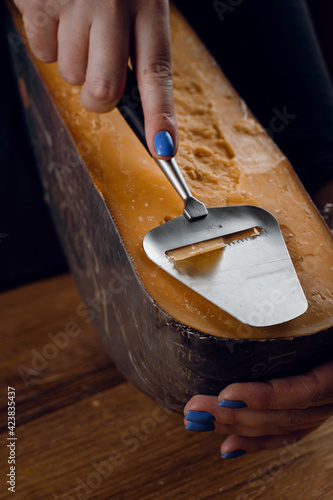Slicing aged cheese parmesan with crystals using a slicer knife. Hard cheese with knife on dark background. Snack tasty piece of food for appetizer