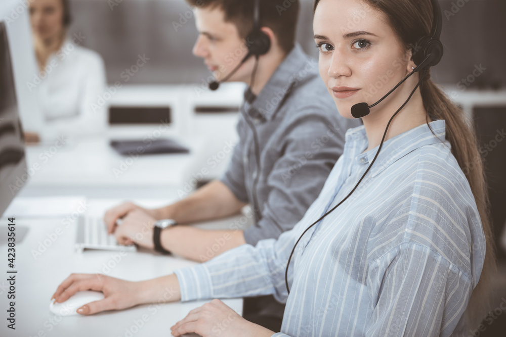 Call center. Group of casual dressed operators at work. Brunette business woman in headset at customer service office Call center. Group of casual dressed operators at work. Brunette business woman in headset at customer service office