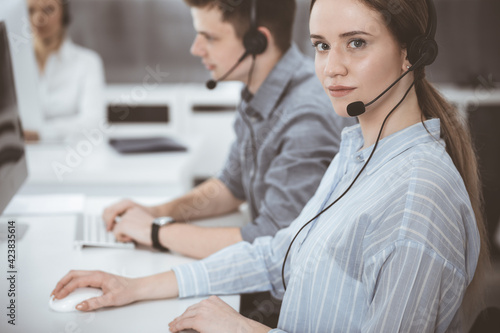 Call center. Group of casual dressed operators at work. Brunette business woman in headset at customer service office