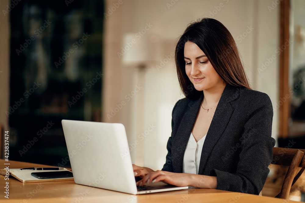 Online foreign language training. Portrait of a beautiful young woman sitting at a wooden table. The assistant works on a laptop computer in the office.Comfortable working space in a coworking space. Online foreign language training. Portrait of a beautiful young woman sitting at a wooden table. The assistant works on a laptop computer in the office.Comfortable working space in a coworking space.