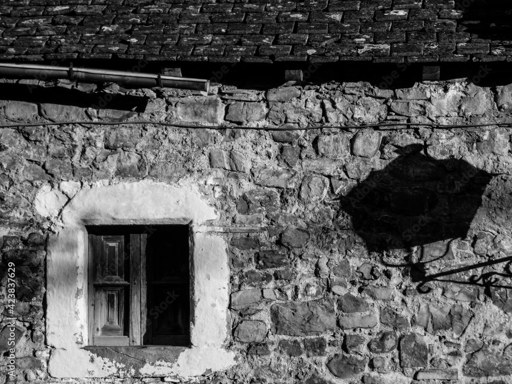 Una fachada de piedra con una ventana enmarcada con moldura encalada y la sombra de una farola en una imagen en blanco y negro de una aldea de montaña del Pirineo español