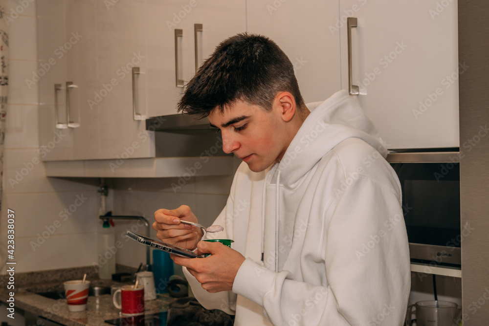 teenager male in kitchen eating breakfast with smartphone teenager male in kitchen eating breakfast with smartphone