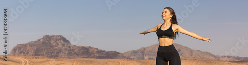 A thin athletic girl takes a break between classes on the background of mountains in the early morning