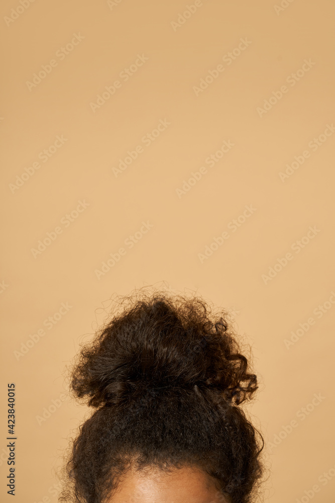 Studio shot of young mixed race woman with highly raised dark curly hair posing isolated over beige background