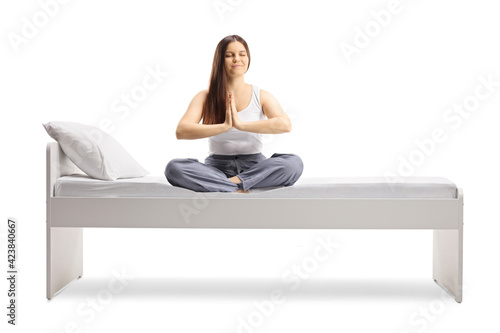 Young female in pajamas sitting on a bed and meditating