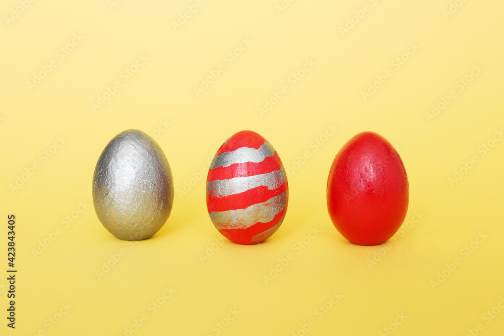 abstract composition of three multi-colored handmade eggs on a yellow pastel background. Eggs of metallic, red, red with gray stripes on a yellow paper background. abstract composition of three multi-colored handmade eggs on a yellow pastel background. Eggs of metallic, red, red with gray stripes on a yellow paper background.
