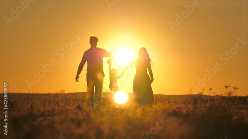 A small child walks with mom and dad at a bright sunset in the sky. Meet the sunrise with your family while traveling. Go hiking with your mother and father. Kid and loving parents walk in the park © Валерий Зотьев