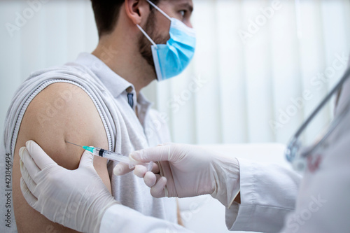 Close up view of young man getting vaccine shot in his arm during corona virus pandemic.
