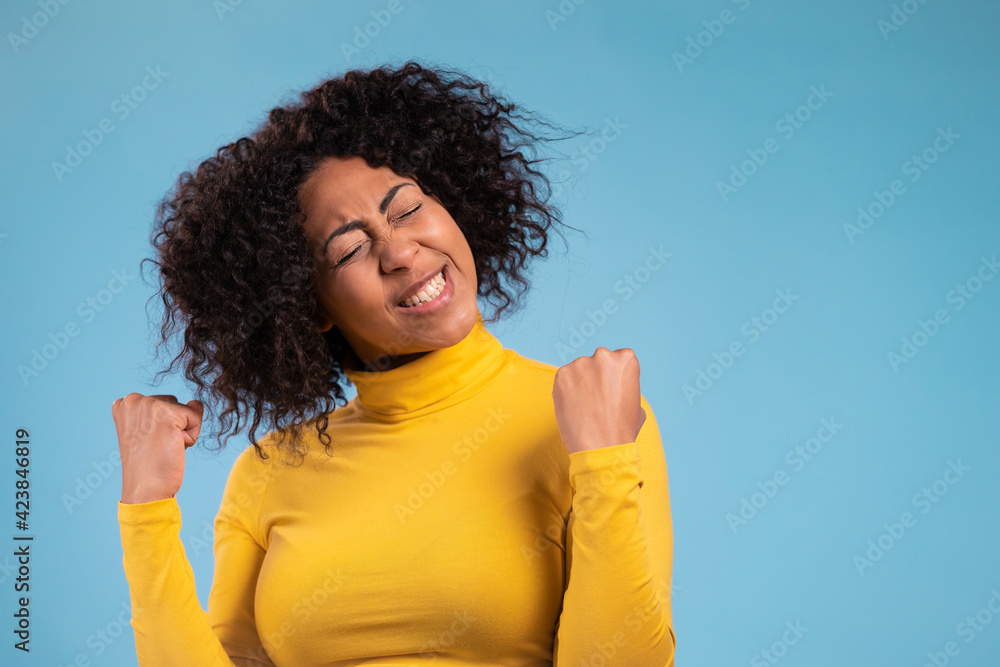 African woman is very glad and happy, she shows yes gesture of victory, she achieved result, goals. Surprised excited happy lady on blue studio background. Jackpot concept. African woman is very glad and happy, she shows yes gesture of victory, she achieved result, goals. Surprised excited happy lady on blue studio background. Jackpot concept.