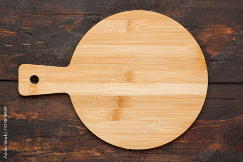 Round wooden cutting board for pizza ondark wooden background. Top view. Mock up for food project. photo