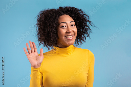 African friendly woman waving hand - hello. Greeting, say Hi to camera. Beautiful young girl on blue studio background. 4k