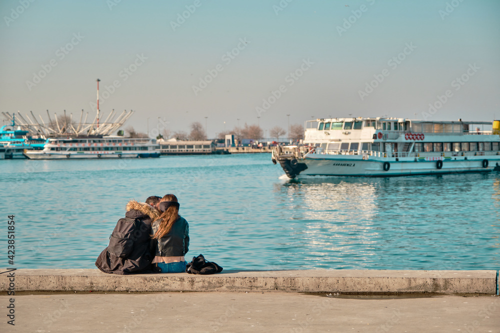 Turkey istanbul 04.03.2021. Two young couples and lovers hugging each other and sitting against bosporus in Kadikoy istanbul during sunny day with passenger ferry and turquoise water background. Turkey istanbul 04.03.2021. Two young couples and lovers hugging each other and sitting against bosporus in Kadikoy istanbul during sunny day with passenger ferry and turquoise water background.