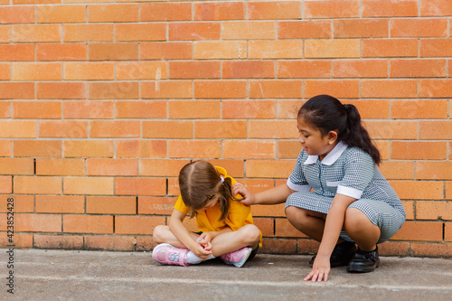 Older school girl comforting younger child who got bullied by classmates