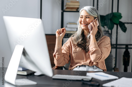 Successful confident beautiful senior gray-haired asian woman, business leader, manager, working at the office, talking on the phone with friends or colleagues, looking away, smiling