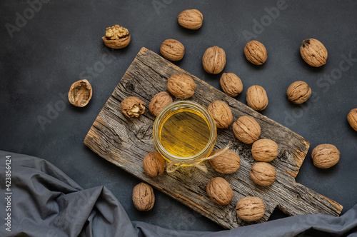 Glass jar of walnut oil with dry walnuts on rustic table